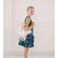 Young girl in a blue dress holding a white tote bag against a light-colored wall.
