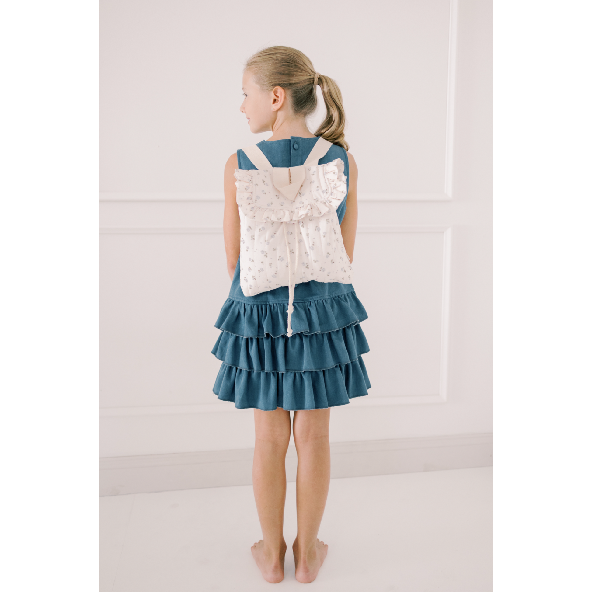 Girl wearing a denim dress with a white lace backpack on a plain background
