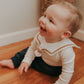 A baby wearing a white sailor-style collar bib with a knotted tie, sitting on the floor.