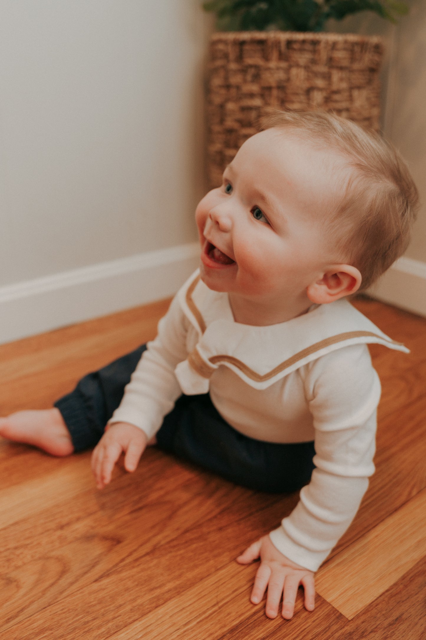 A baby wearing a white sailor-style collar bib with a knotted tie, sitting on the floor.