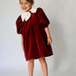 Young girl wearing a red velvet dress with white collar against a plain background