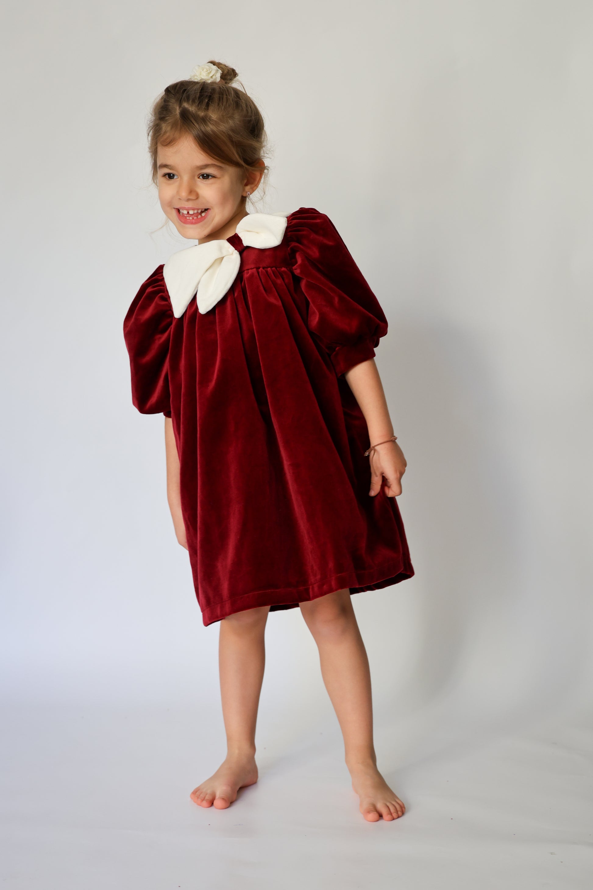Young girl wearing a red velvet dress with white collar against a plain background