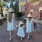 Three sisters in matching dresses and hats walking together on a brick path in front of a brick building.