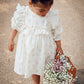 Child in a white dress holding a bouquet of flowers on a textured surface