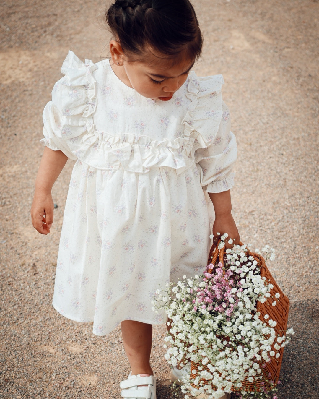 Child in a white dress holding a bouquet of flowers on a textured surface