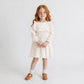 Young girl wearing a white dress with long sleeves on a plain background