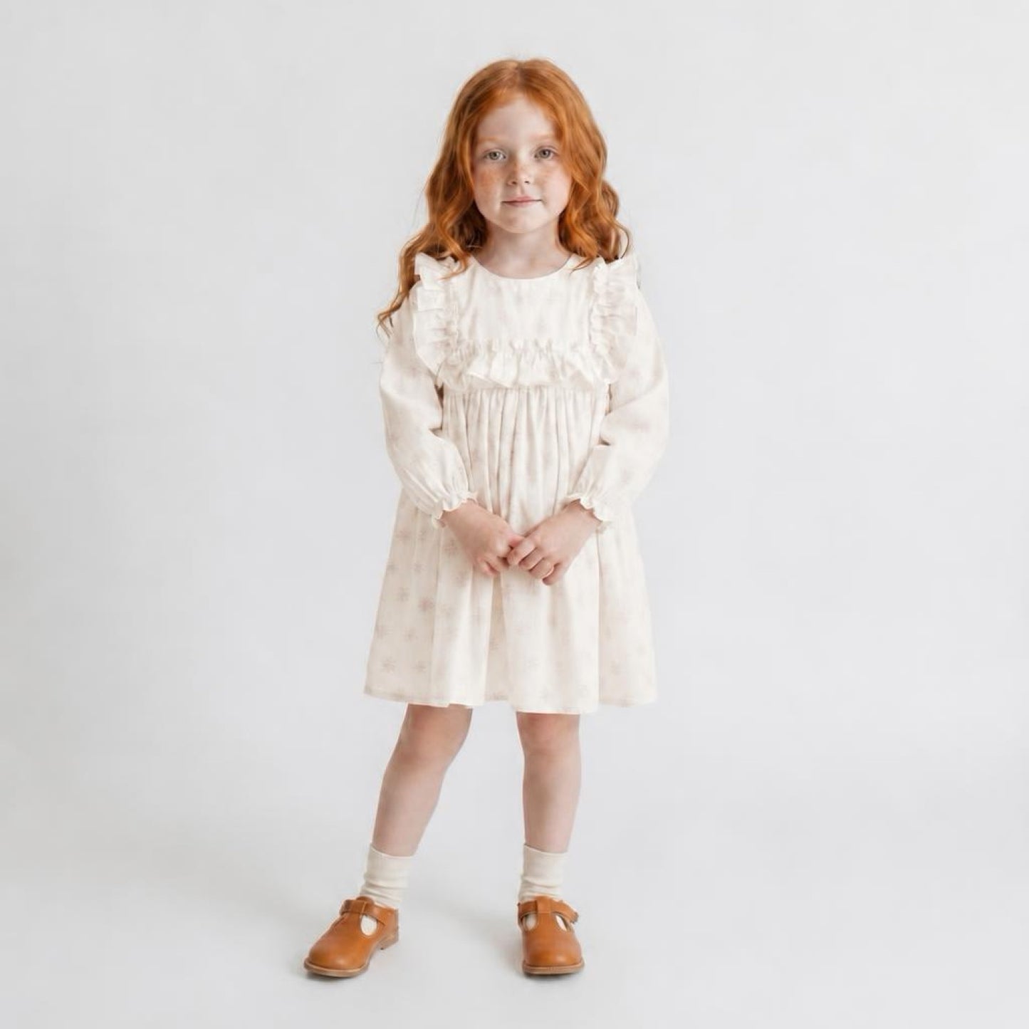 Young girl wearing a white dress with long sleeves on a plain background