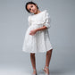 Young girl wearing a white dress with ruffled details on a gray background