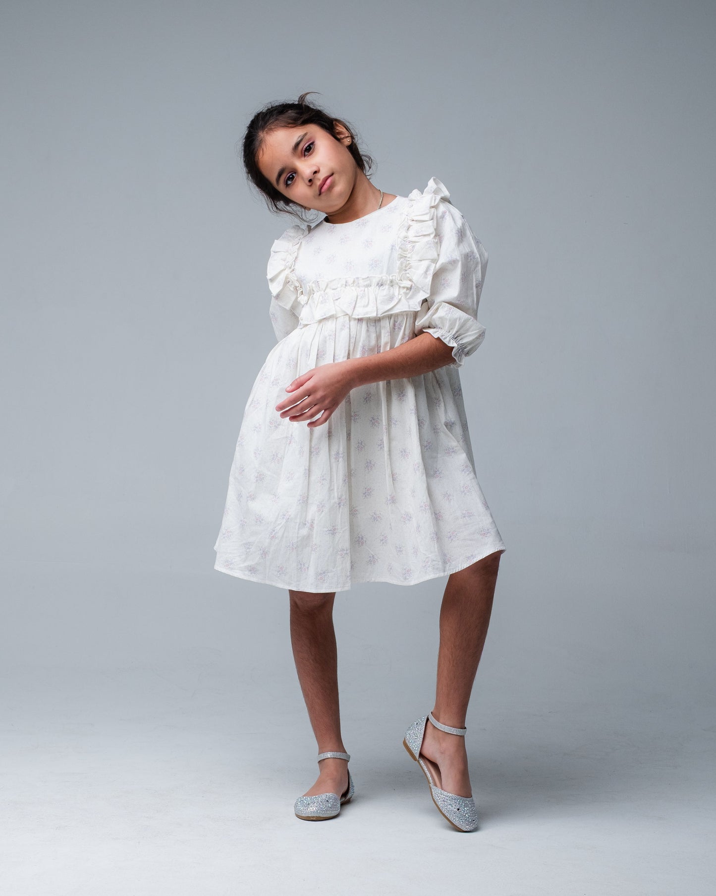 Young girl wearing a white dress with ruffled details on a gray background