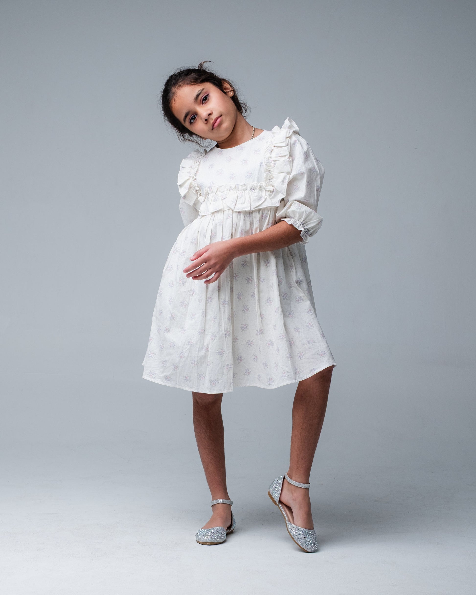 Young girl wearing a white dress with ruffled details on a gray background