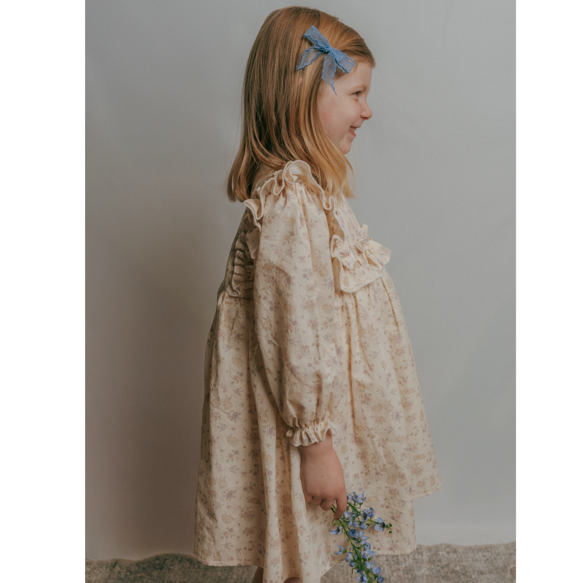 A child wearing a long-sleeved floral dress with a garden hops pattern and ruffles along the bodice.
