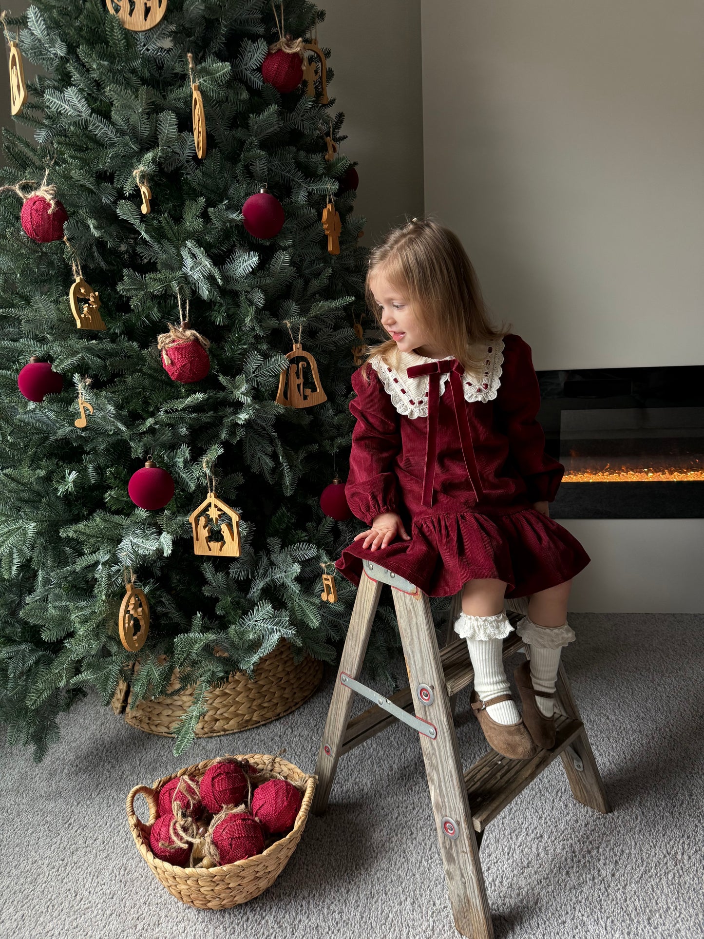 Child decorating a Christmas tree with ornaments on a ladder.