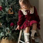Child in a red dress sitting on a ladder next to a decorated Christmas tree.