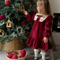 Child in a red dress standing next to a decorated Christmas tree.