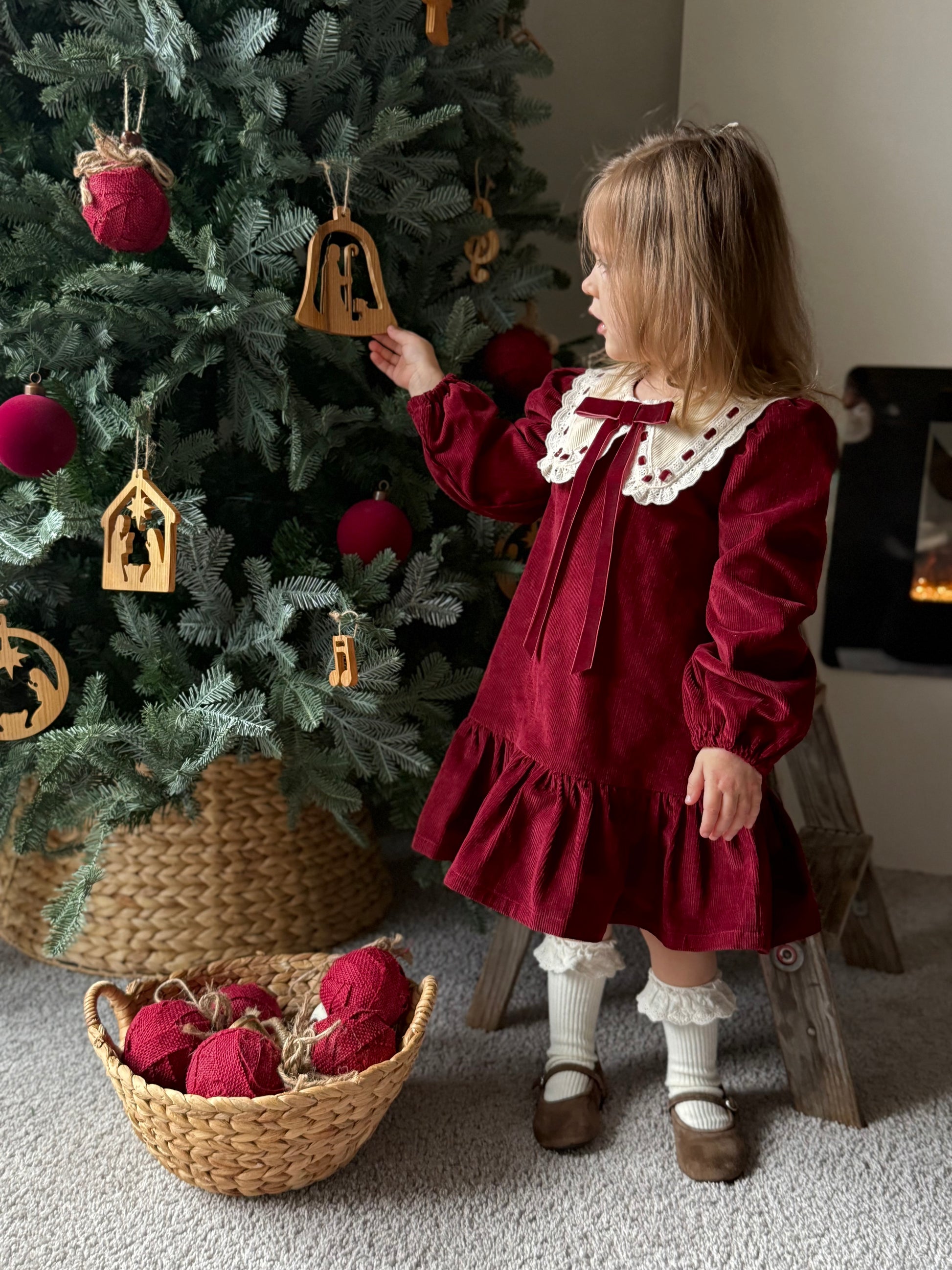 Child in a red dress standing next to a decorated Christmas tree.