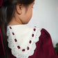 Close-up of a girl wearing a maroon garment with a white lace collar against a neutral background