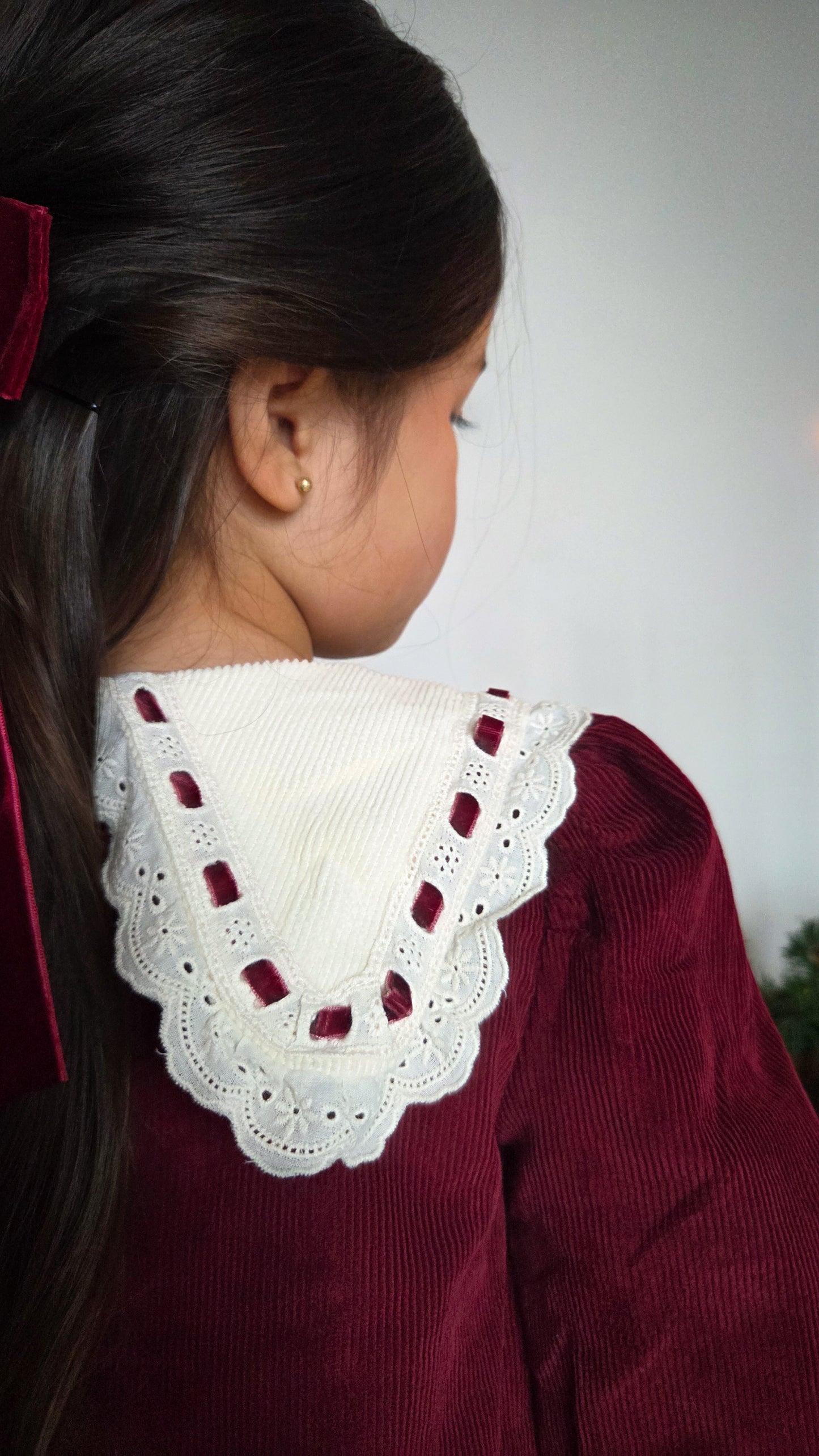 Close-up of a girl wearing a maroon garment with a white lace collar against a neutral background