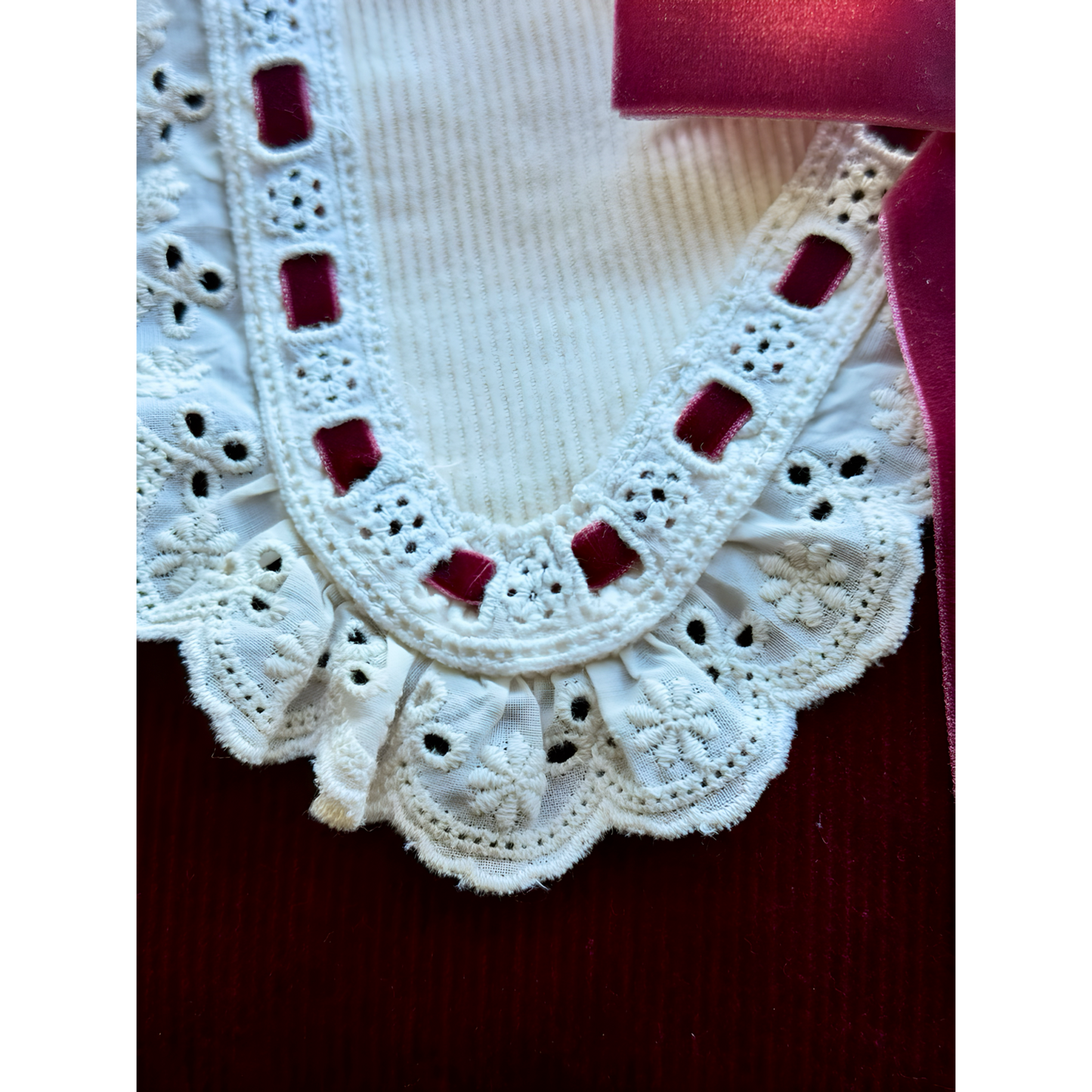Close-up of a white lace collar with red accents on a dark background