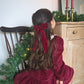 Child in a red dress sitting by a Christmas tree with candles in the background