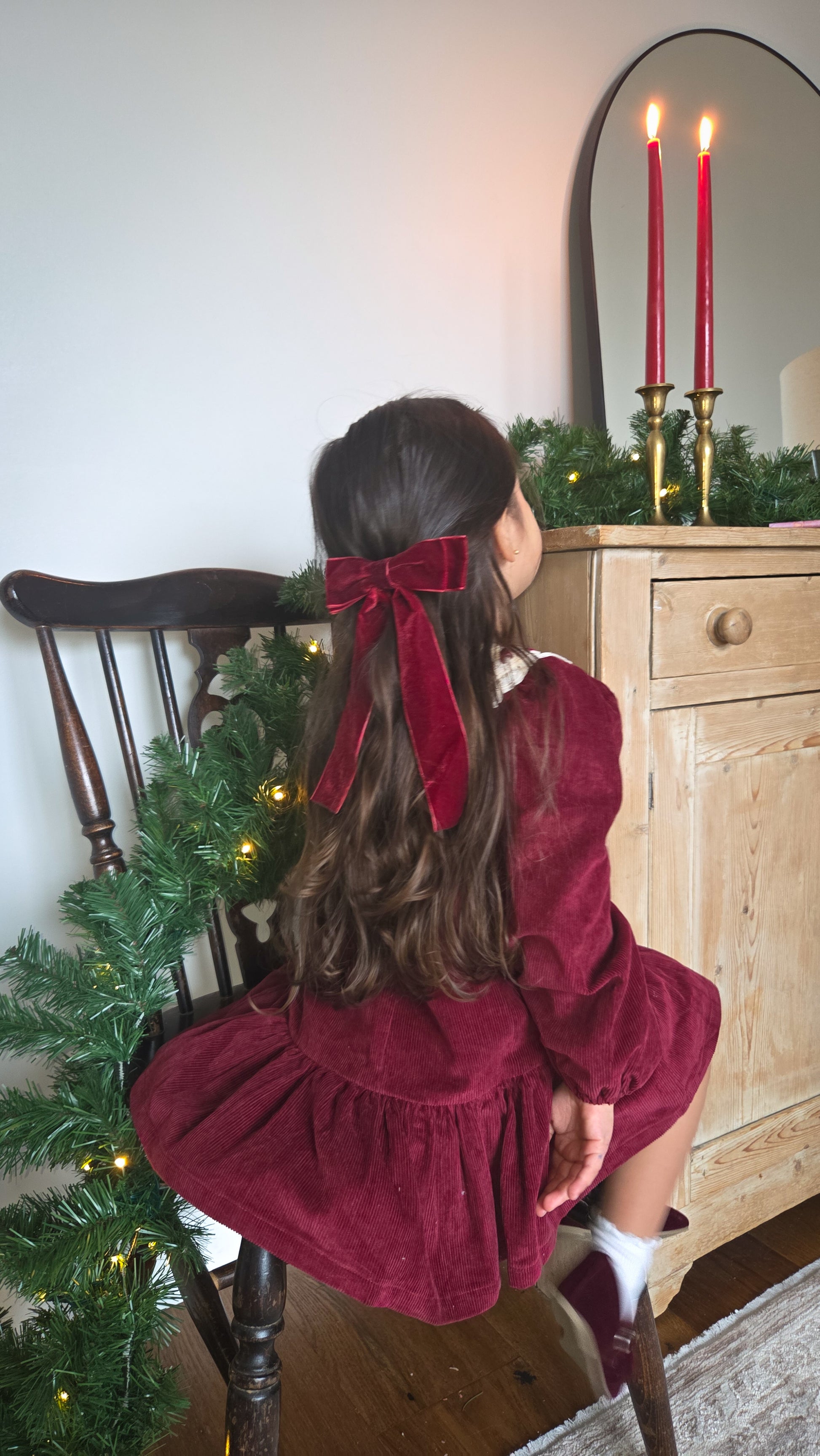 Child in a red dress sitting by a Christmas tree with candles in the background