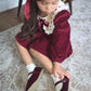 Young girl in a burgundy dress sitting on a patterned rug.