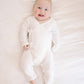 A baby lying on a white textured blanket, wearing a white ribbed long-sleeve footless bodysuit with side ties.