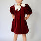 Young girl wearing a red velvet dress with a white collar against a plain background