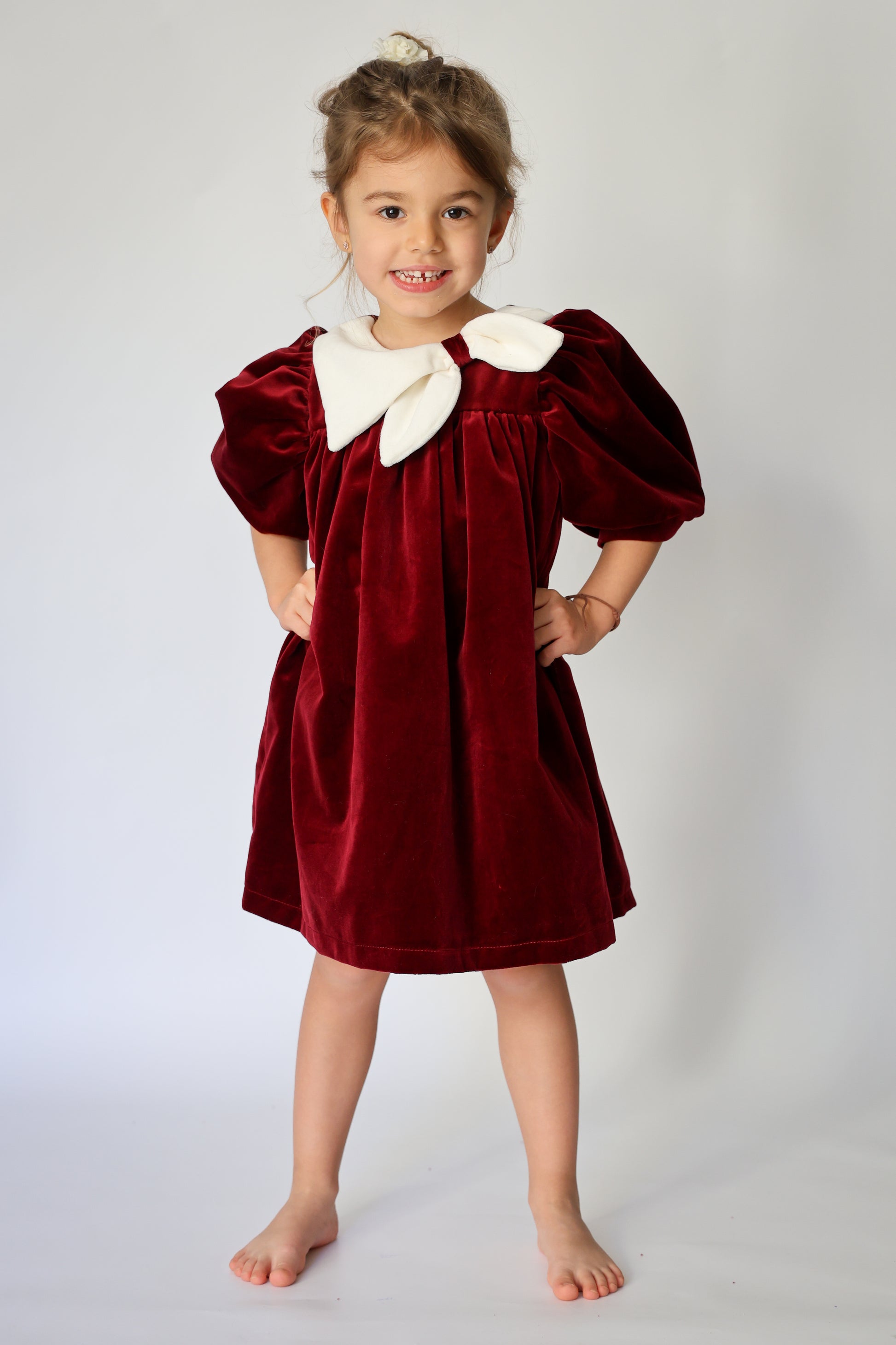 Young girl wearing a red velvet dress with a white collar against a plain background