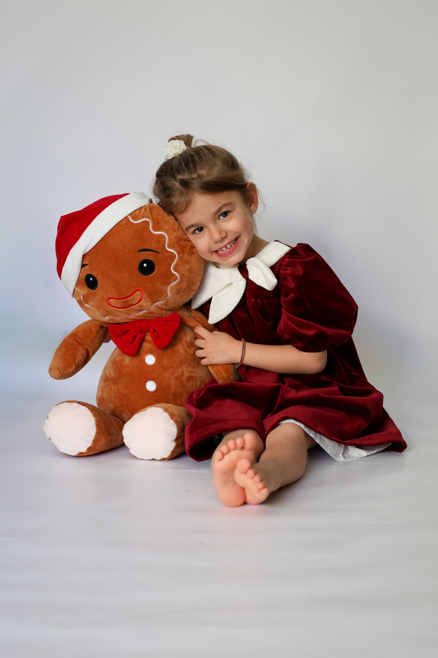 Child in a red dress holding a gingerbread man plush toy against a white background