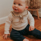 A baby wearing a brown sailor-style collar bib with a knotted tie.