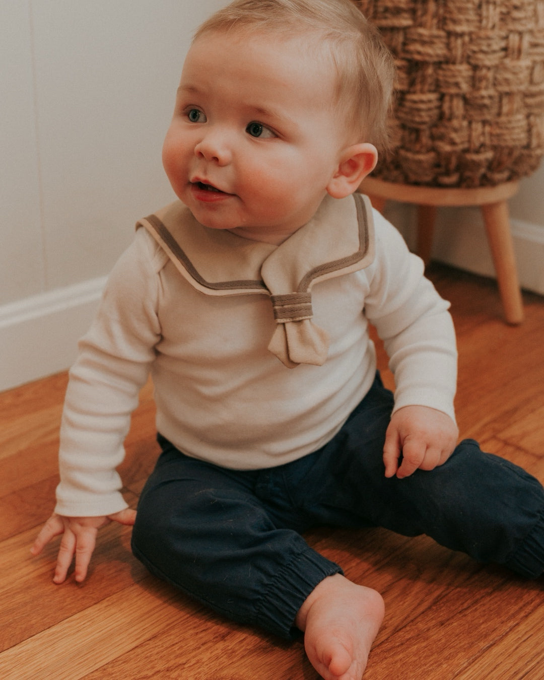 A baby wearing a brown sailor-style collar bib with a knotted tie.