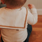 A baby wearing a White sailor-style collar bib with a knotted tie.