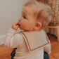 A baby wearing a brown sailor-style collar bib with a knotted tie.