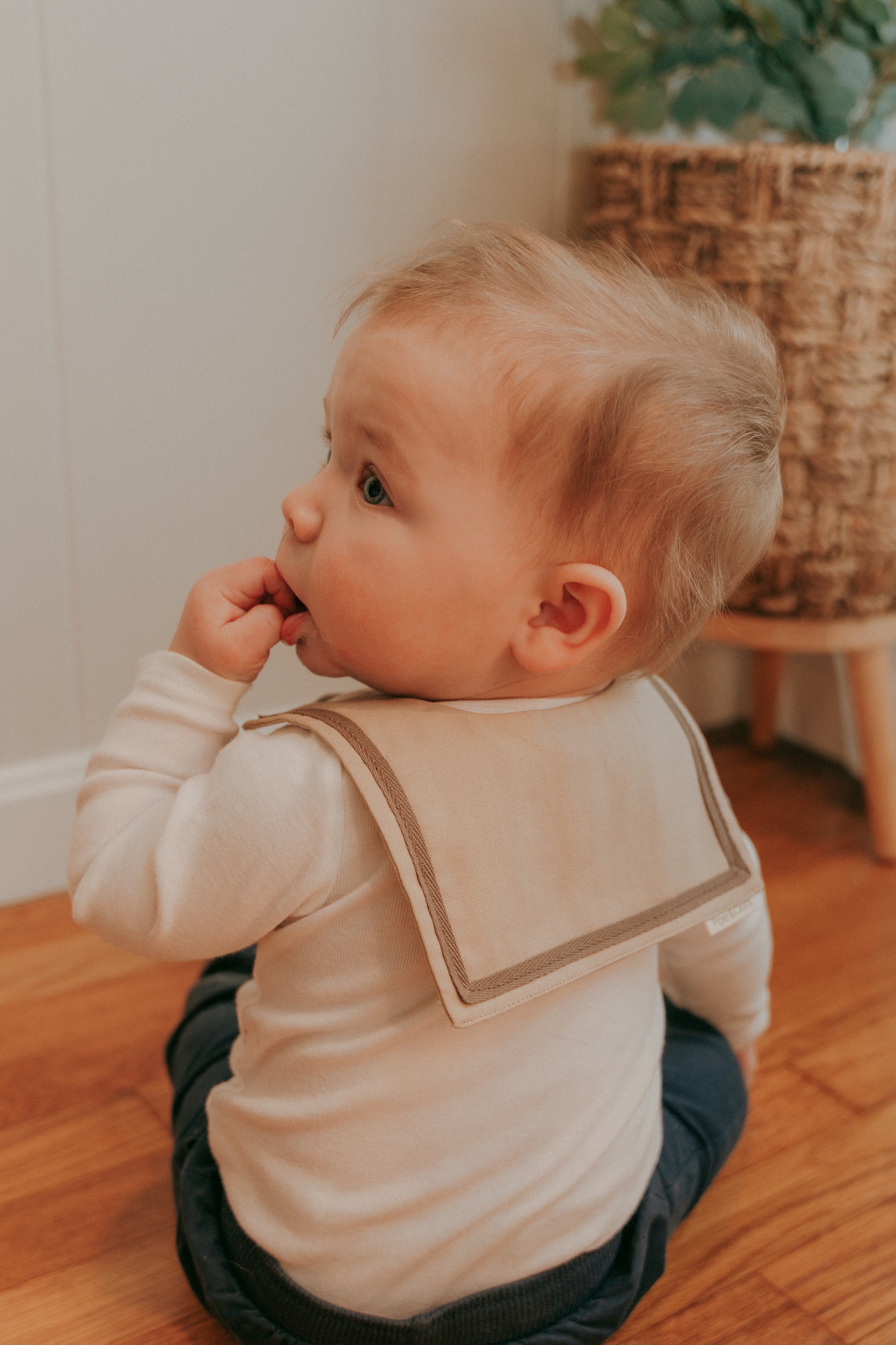 A baby wearing a brown sailor-style collar bib with a knotted tie.