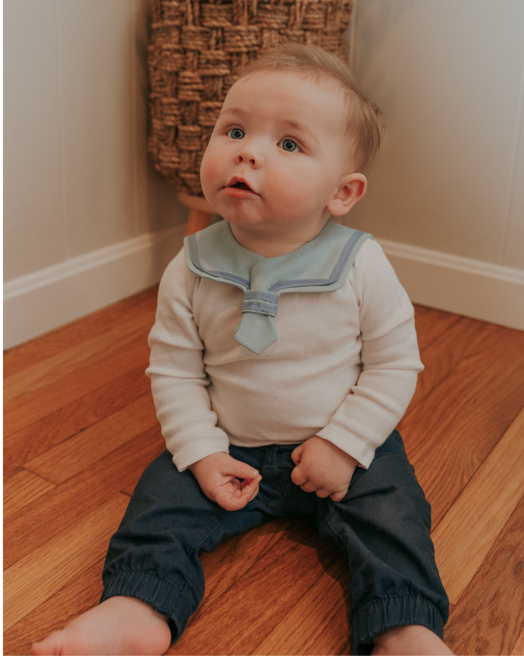 A baby wearing a navy blue sailor-style collar bib with a knotted tie in the front.
