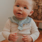 A baby wearing a navy blue sailor-style collar bib with a knotted tie in the front.