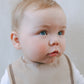A baby wearing a brown sailor-style collar bib with a knotted tie.