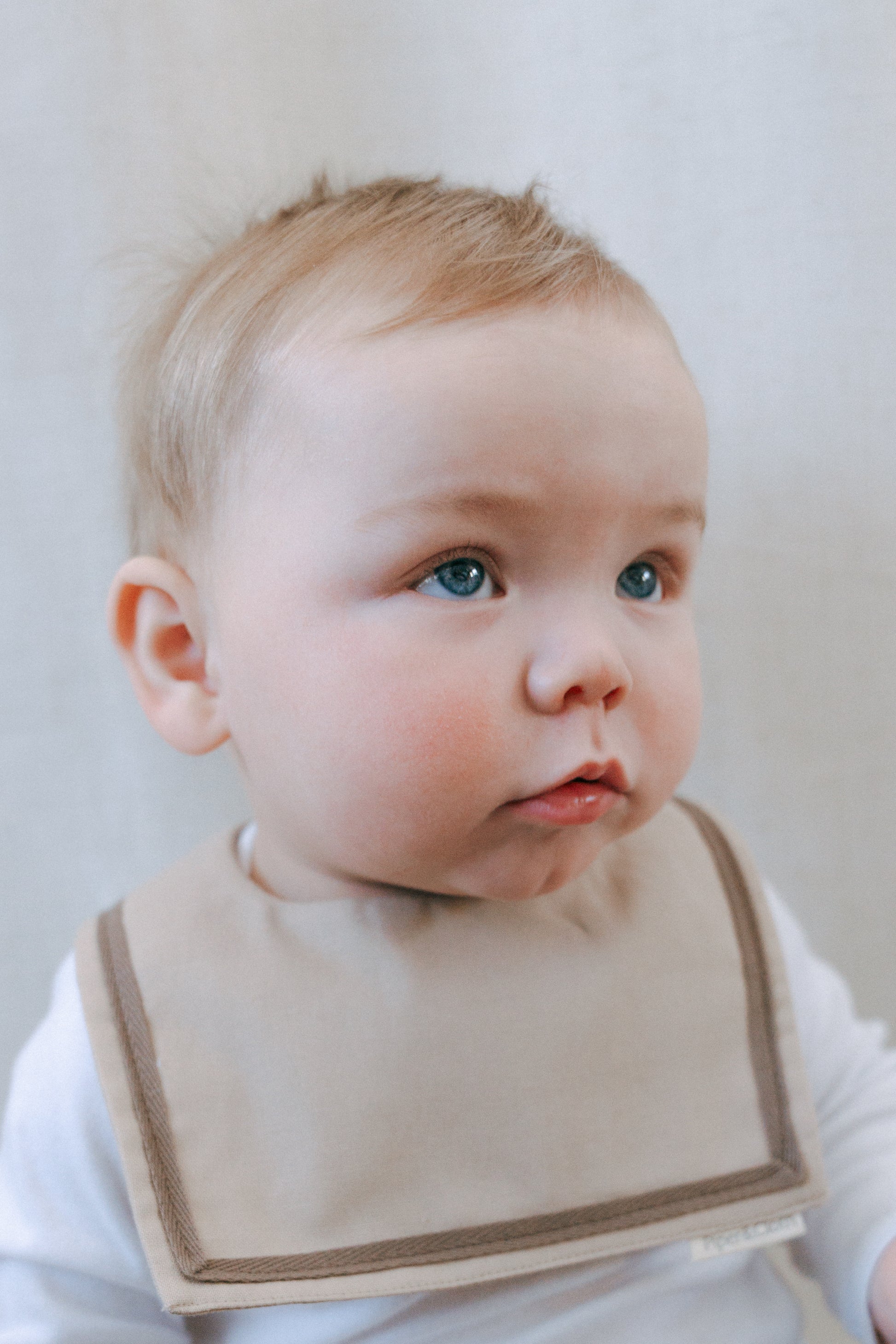 A baby wearing a brown sailor-style collar bib with a knotted tie.