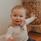A baby wearing a brown sailor-style collar bib with a knotted tie.