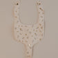 A beige cotton bib with a rosebud print and a pacifier snap, displayed against a neutral background.