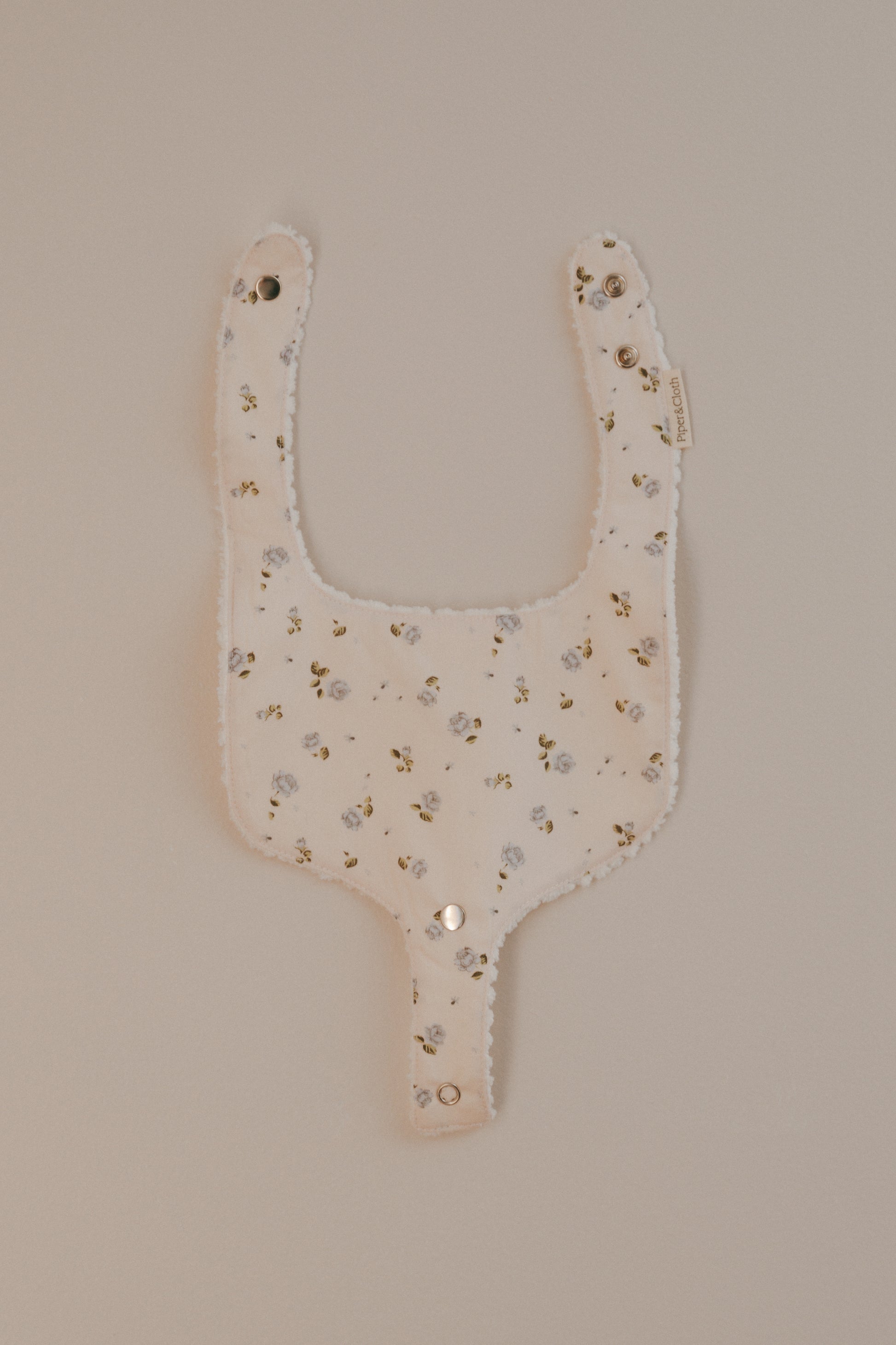 A beige cotton bib with a rosebud print and a pacifier snap, displayed against a neutral background.