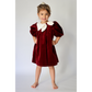 Young girl wearing a burgundy velvet dress with white collar against a plain background