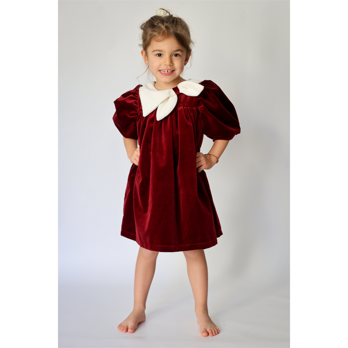 Young girl wearing a burgundy velvet dress with white collar against a plain background