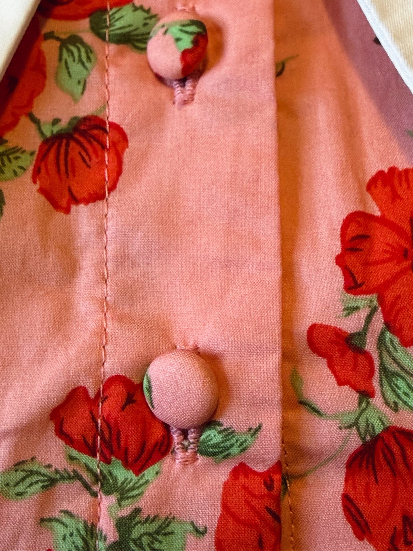 Close-up of a pink fabric with red floral patterns and buttons.