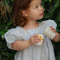 Child in a light dress holding a cup and saucer against a green leafy background