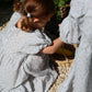 Child in a light gray dress interacting with a stone statue outdoors.