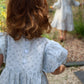 Two children in light blue dresses standing in a garden.