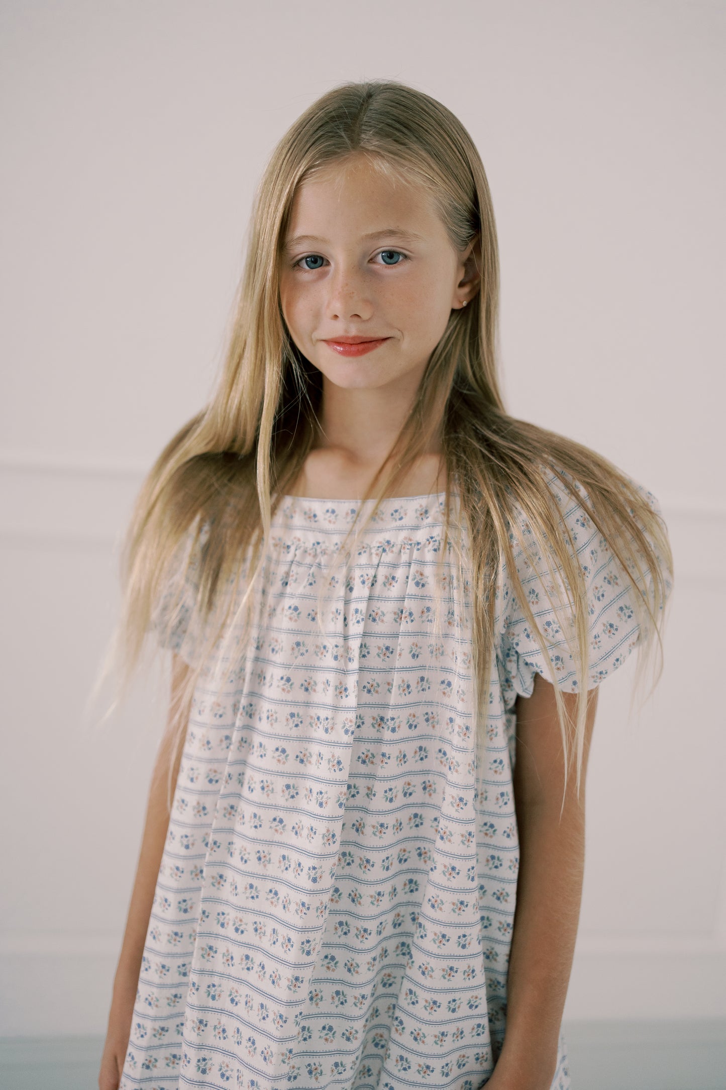 Young girl wearing a light blue floral dress against a plain background