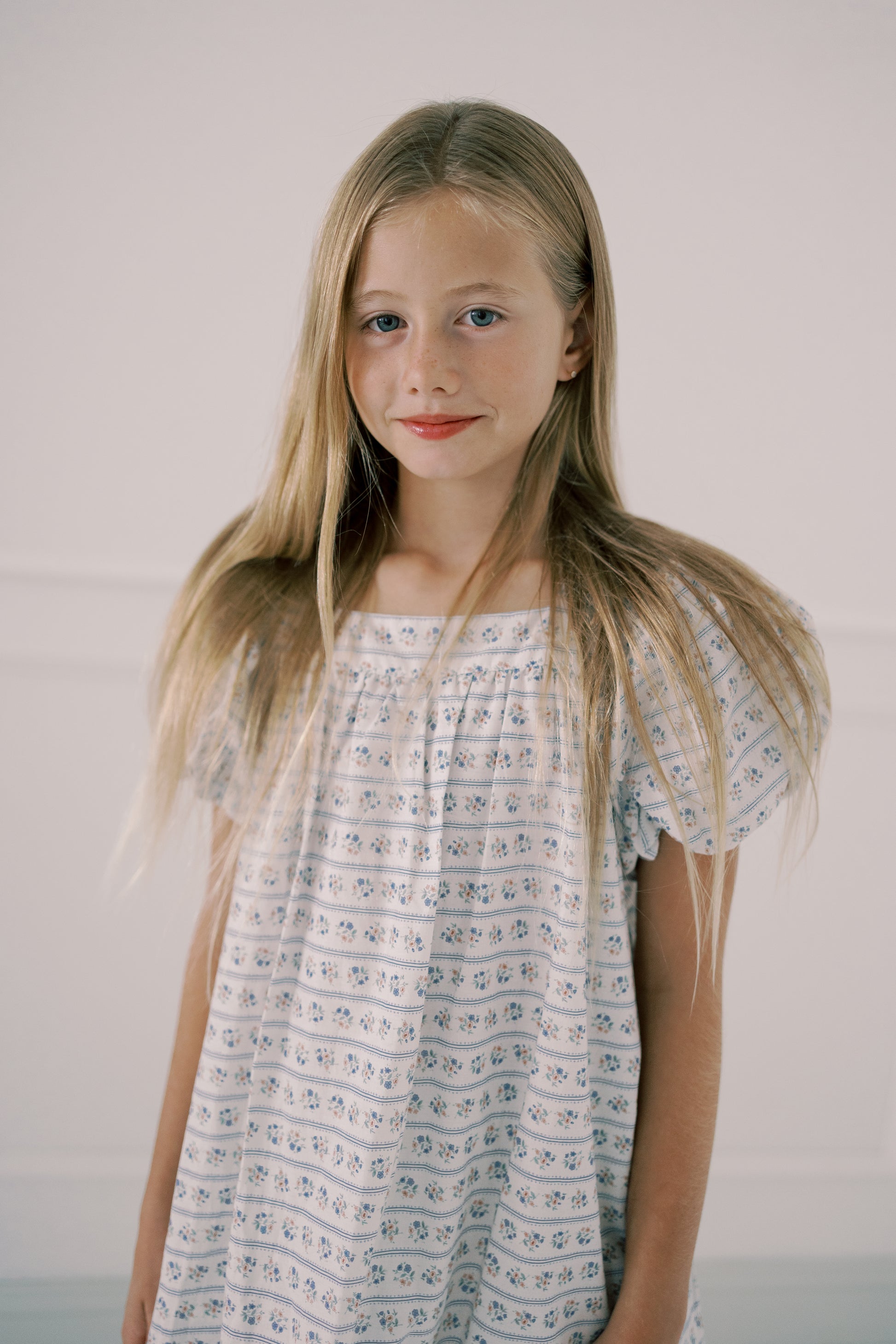 Young girl wearing a light blue floral dress against a plain background