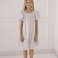Young girl wearing a patterned dress standing against a white wall.